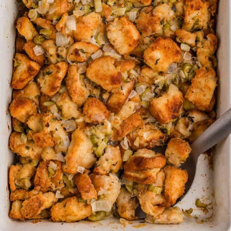Golden brown bread stuffing bake with visible herbs and sausage crumbles in a glass baking dish